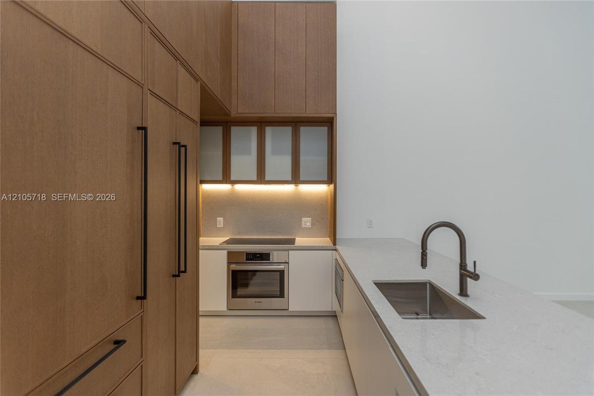 Kitchen featuring full-height wood-finish cabinetry, white solid surface countertops, a stainless steel wall oven, an integrated cooktop, and an under