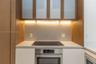 Kitchen area featuring matte white base cabinetry, integrated stainless steel oven, cooktop, solid-surface countertop, and wood-finish upper cabinets 