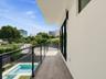 Balcony featuring wood-finish flooring, a glass-panel railing with metal framing, and exterior wall-mounted lighting