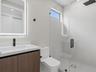 Modern vanity featuring a stone countertop, integrated sink, and illuminated mirror, paired with a glass-enclosed shower with matte black rainfall sho