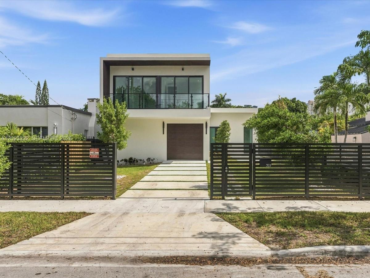 Modern residence featuring a flat-roof exterior, a second-story glass balcony, a concrete paver driveway, and a horizontal-slat metal perimeter fence