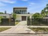 Modern residence featuring a flat-roof exterior, a second-story glass balcony, a concrete paver driveway, and a horizontal-slat metal perimeter fence
