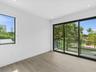 Wood-finish flooring, sliding glass doors with black frames, recessed ceiling lighting, and a glass-paneled balcony