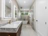 Dual-sink vanity with stone countertop and integrated lighting, walk-in glass shower enclosure, freestanding soaking tub, and metallic gold-finish fix