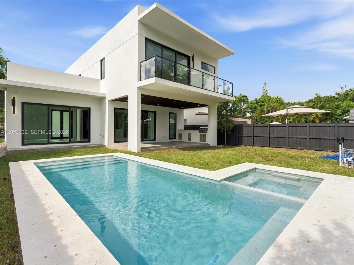 Modern exterior featuring a geometric stucco facade, a second-story balcony with glass railing, a covered patio with built-in outdoor kitchen, and a s