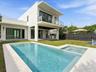 Modern exterior featuring a geometric stucco facade, a second-story balcony with glass railing, a covered patio with built-in outdoor kitchen, and a s