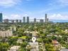 Aerial perspective featuring a residential lot with a swimming pool, mature canopy trees, and high-rise urban skyline scenery