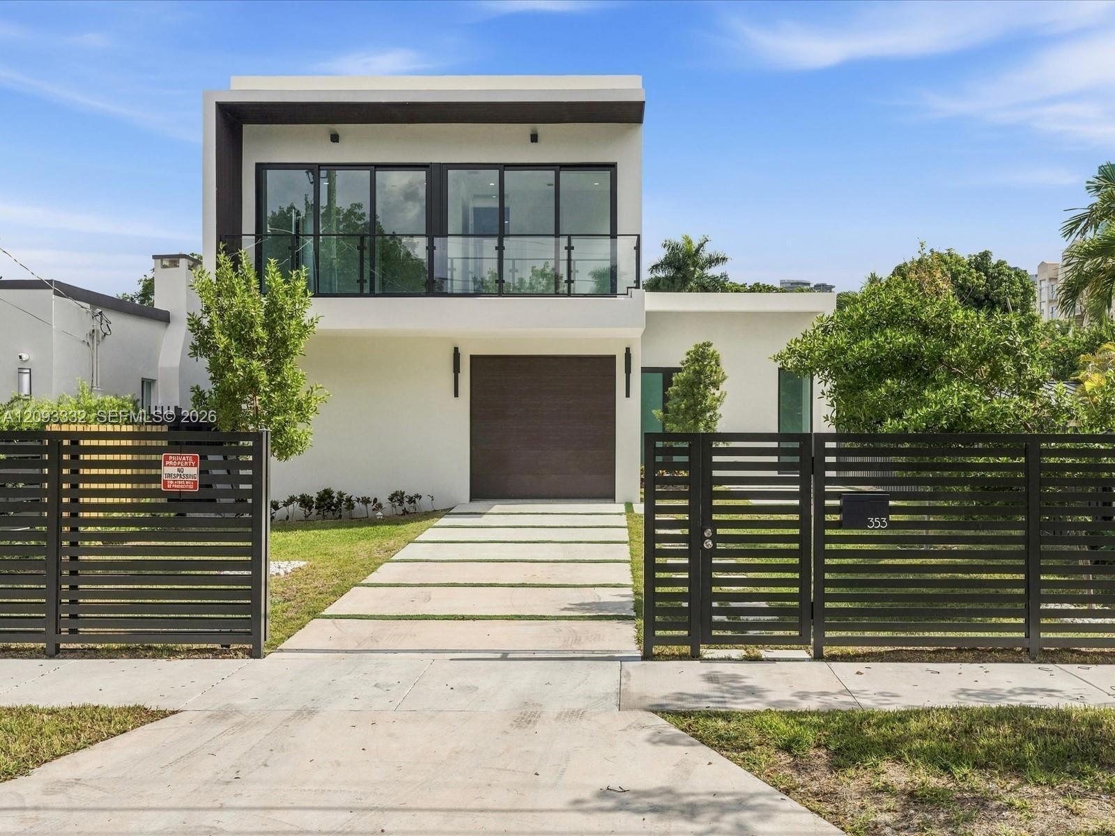 Modern two-story exterior featuring a glass-railed balcony, horizontal slat fencing, a segmented concrete driveway, and a solid-panel garage door