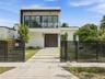 Modern two-story exterior featuring a glass-railed balcony, horizontal slat fencing, a segmented concrete driveway, and a solid-panel garage door
