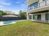 Modern architectural exterior featuring a second-story balcony with glass railings, a covered ground-level patio, an integrated swimming pool with a s