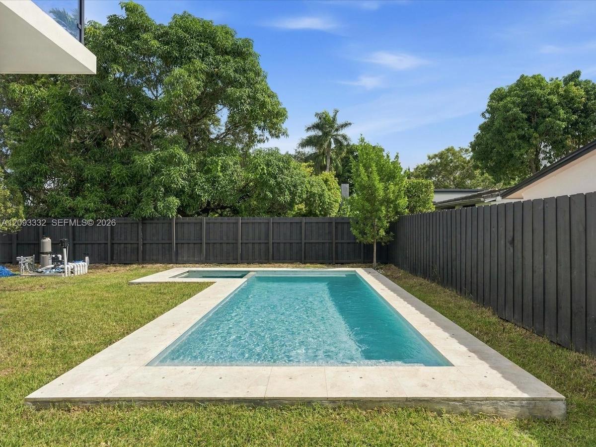 In-ground swimming pool featuring a built-in spa, stone-finish pool decking, manicured lawn, and privacy fencing