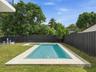 In-ground swimming pool featuring a built-in spa, stone-finish pool decking, manicured lawn, and privacy fencing
