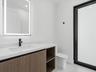 Wood-finish floating vanity with white stone countertop, rectangular undermount sink, matte black faucet, integrated LED-backlit mirror, and matte bla