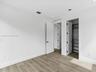 Neutral-toned wood-finish flooring, crisp white walls, minimalist shaker-style interior doors with matte black hardware, and an integrated reach-in cl