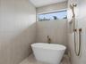 Freestanding soaking tub featuring a metallic bronze floor-mounted faucet, textured stone-finish wall tile, a recessed wall niche, and a metallic bron