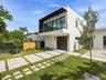 Modern stucco exterior featuring a cantilevered balcony, dark-tinted glass railings, multi-panel sliding doors, and a decorative concrete paver drivew