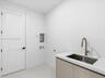 Utility area featuring a neutral-toned vanity with a stone-surface countertop, an integrated stainless steel drop-in sink, a high-arc faucet, and a wh
