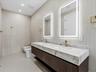 Floating dual-sink vanity featuring stone countertops, dark wood-finish cabinetry, integrated LED-backlit mirrors, and brass fixtures
