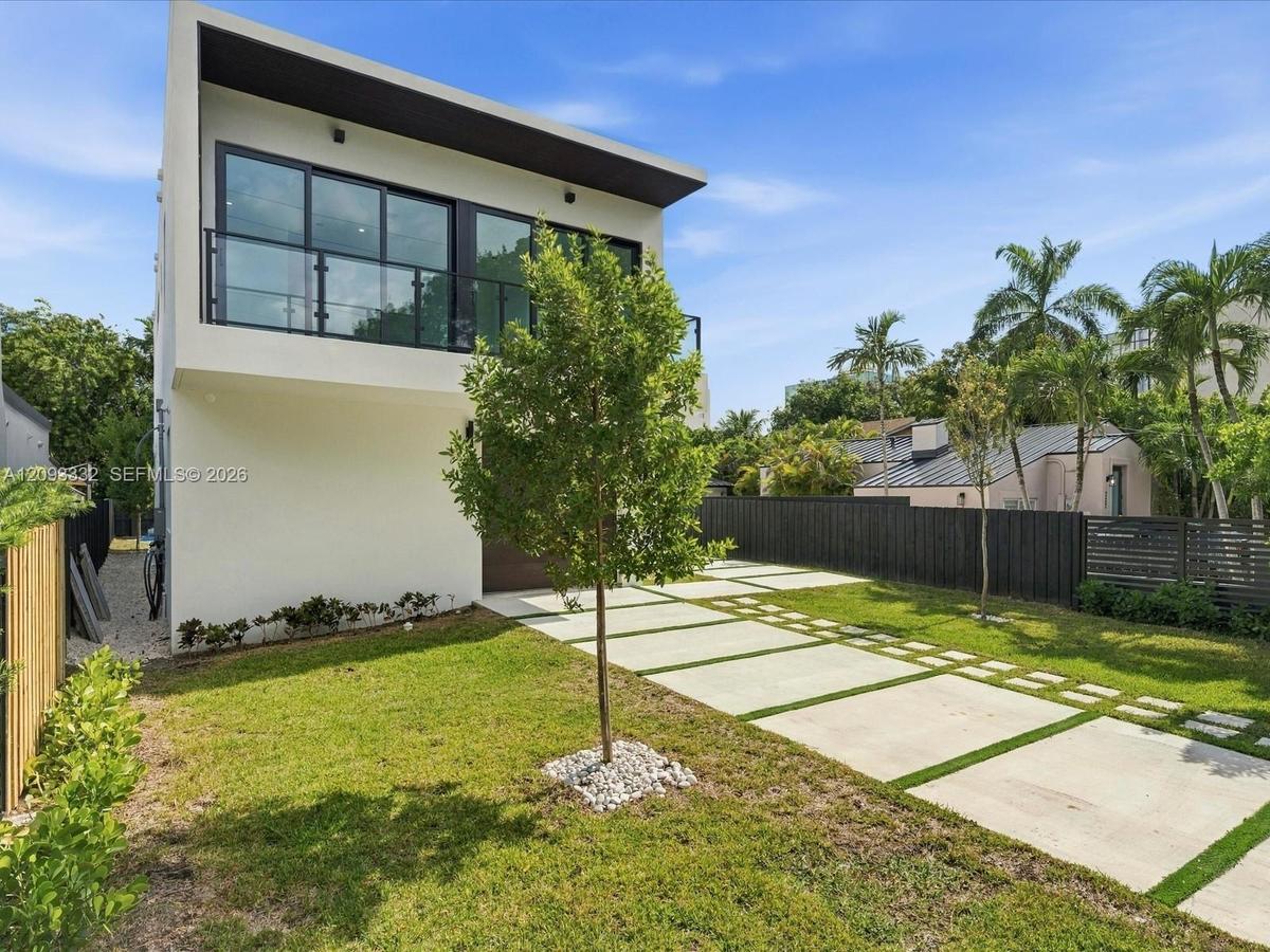 Modern exterior featuring a smooth stucco finish, upper-level balcony with metal railing, flat roofline, oversized sliding glass doors, and a concrete