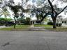 Single-story residence featuring a brick-paved walkway, mature canopy trees, manicured hedges, and an attached garage