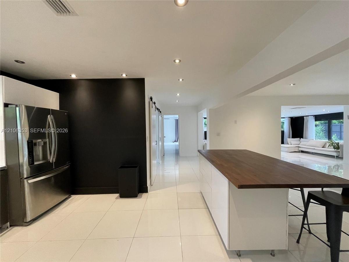 Kitchen featuring a white cabinetry island with a wood-finish countertop, high-gloss large-format tile flooring, stainless steel refrigerator, and rec