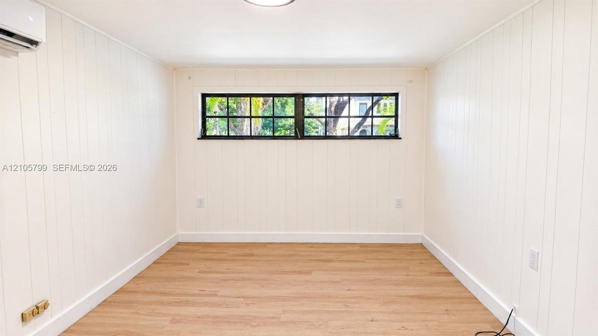 Interior space featuring vertical wood-paneled walls, wood-finish flooring, a wall-mounted ductless climate control unit, and a horizontal multi-pane 
