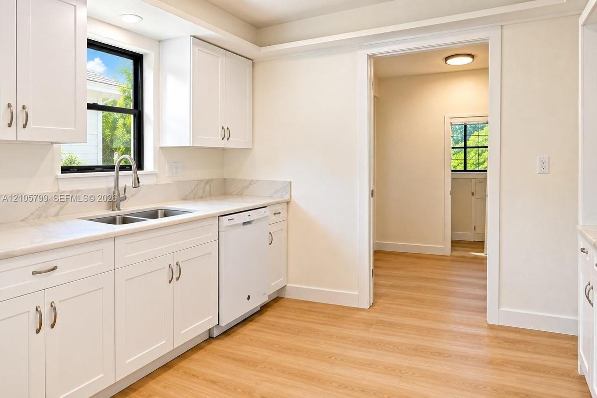 Kitchen featuring white shaker-style cabinetry, stone-patterned backsplash, light-toned wood-finish flooring, undermount dual-basin sink, and recessed