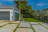 Modern exterior featuring a smooth stucco finish, large-format concrete paver driveway with turf inlays, manicured synthetic grass lawn, mature palm t