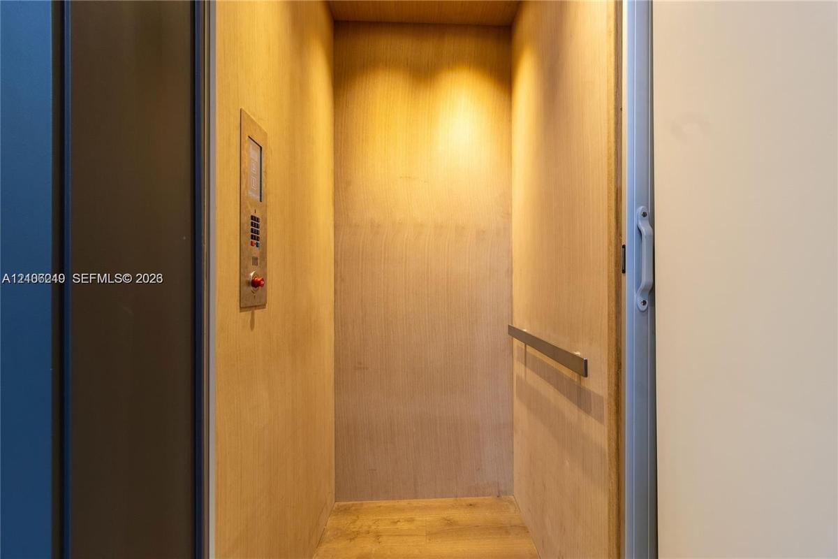 Private elevator featuring wood-paneled walls, wood-finish flooring, a stainless steel control panel, and a horizontal metal handrail