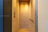 Private elevator featuring wood-paneled walls, wood-finish flooring, a stainless steel control panel, and a horizontal metal handrail