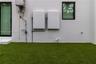 Exterior wall featuring dual Tesla Powerwall energy storage units, an on-demand tankless water heater, and artificial turf surfacing