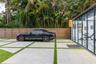 Large-format concrete paver driveway with turf infill, horizontal wood privacy fencing, and floor-to-ceiling glass wall panels