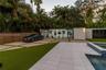 Contemporary pool deck featuring large-format stone pavers, integrated glass-walled studio structure, geometric concrete driveway with turf inserts, a