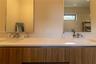 Double vanity featuring a light-toned solid surface countertop, wood-finish cabinetry, two undermount sinks with polished chrome faucets, and dual int