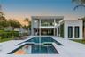 Modern multi-level exterior featuring a glass-railed balcony, ground-level covered patio, integrated pool and spa, and vertical green wall accents