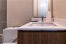 Modern vanity featuring wood-finish cabinetry, a white countertop with an integrated rectangular sink, chrome fixtures, and a frameless mirror