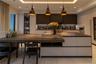 Modern kitchen featuring dark-toned cabinetry, a substantial kitchen island with an integrated dining surface, recessed ceiling lighting, three suspen