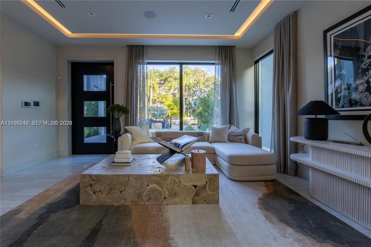 Tray ceiling with recessed perimeter lighting, floor-to-ceiling windows, modern black multi-panel entry door, and light-toned flooring