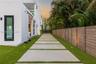 Modern exterior featuring smooth white stucco, a geometric concrete paver pathway, artificial turf landscaping, a horizontal wood-slat privacy fence, 