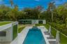 Outdoor space featuring an in-ground swimming pool with integrated spa, white stone pool deck, synthetic lawn, and a detached structure with metal roo