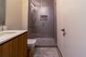 Wood-finish vanity cabinet with a white countertop and integrated sink, glass-enclosed shower featuring tiled walls, built-in recessed shelving, a rai