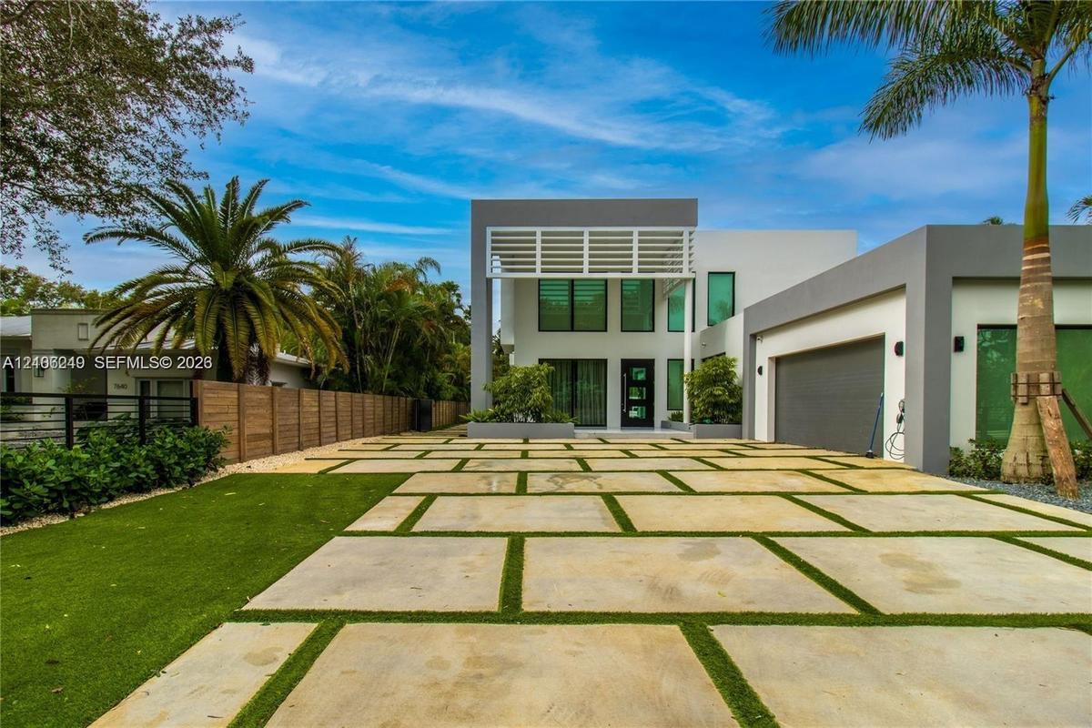 Modern architectural exterior featuring a concrete paver driveway with integrated turf, two-story facade with expansive glass windows, and a structure