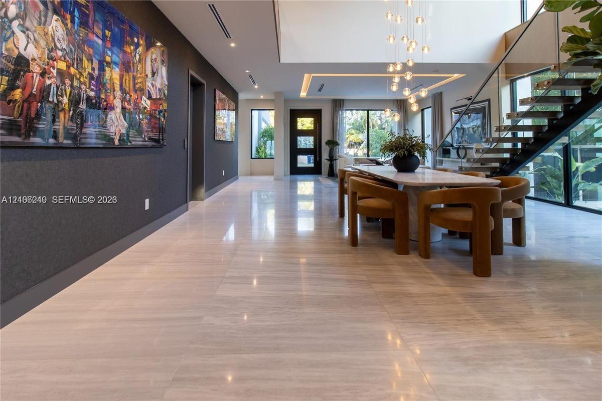Open-concept interior featuring large-format tile flooring, a double-height ceiling with recessed cove lighting, and a suspended staircase with glass 