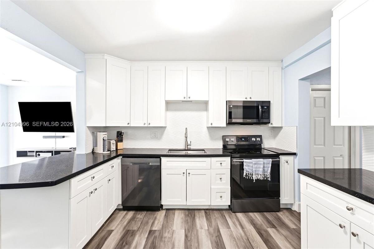 Kitchen featuring white shaker-style cabinetry, dark stone-finish countertops, black appliances, a textured tile backsplash, and wood-finish flooring