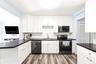 Kitchen featuring white shaker-style cabinetry, dark stone-finish countertops, black appliances, a textured tile backsplash, and wood-finish flooring