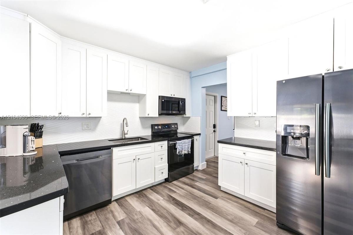 Kitchen featuring white cabinetry, dark stone-finish countertops, textured tile backsplash, stainless steel appliances, and wood-finish flooring