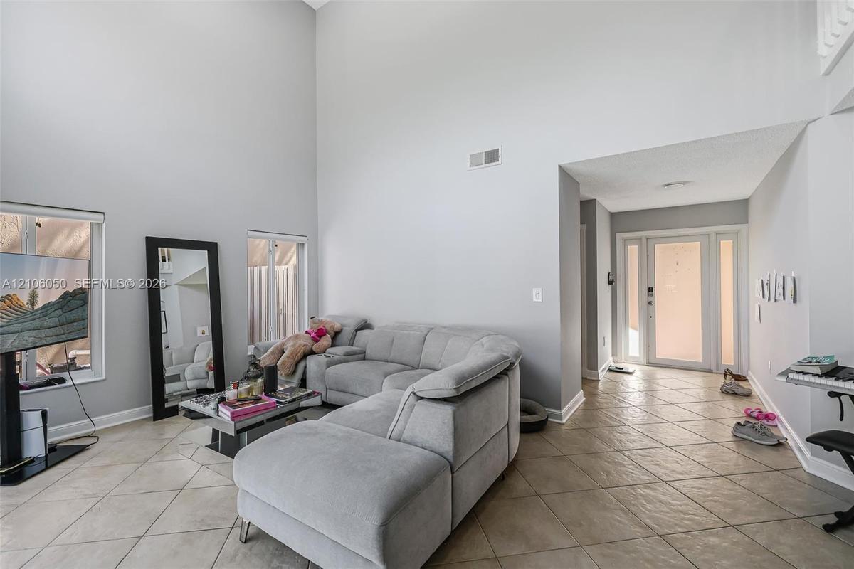 High-ceilinged room featuring ceramic tile flooring, dual windows, and an entryway with a glass-panel door and sidelights