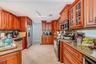 Kitchen featuring stained wood cabinetry with glass-panel upper doors, stone-finish countertops, stainless steel appliances, and ceramic tile flooring