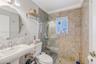 Bathroom featuring a wall-mounted oval mirror, porcelain pedestal sink, chrome hardware, and a glass-enclosed walk-in shower finished with full-height