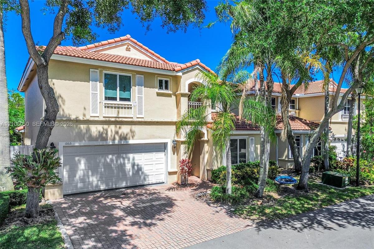 Stucco exterior featuring a clay tile roof, arched entryway, brick-paver driveway, and an attached two-car garage